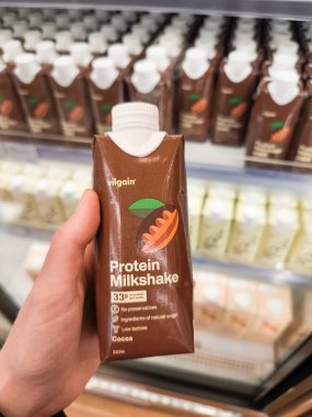 Prag, Çek Cumhuriyeti - 30 Nisan 2025: Vilgain Hand, benzer ürünlerle dolu soğutulmuş bir rafın önünde bir süpermarkette kakao proteinli milkshake tutuyor.