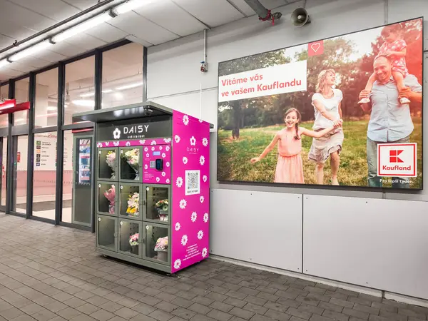 Prag, Çek Cumhuriyeti - 30 Nisan 2025: Çeşitli buketler dağıtan Daisy Flower mağaza otomatı Kaufland yakınlarındaki bir kamu alanında mutlu bir ailenin yer aldığı bir reklamın yanında oturuyor