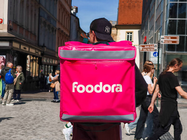 Prague, Czech republic - April 30, 2025: Food delivery driver foodora walking on wenceslas square in prague, czech republic, carrying a pink thermal bag