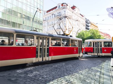 Prag, Çek Cumhuriyeti - 30 Nisan 2025: Biri kırmızı, biri bej olmak üzere iki tramvay güneşli bir günde yolcu taşıyan Prag, Czechia 'da bir kavşakta buluşuyor.