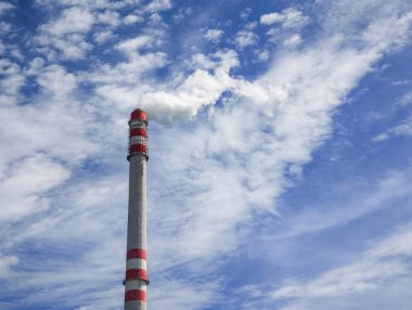 Prag 'daki hava kirliliğini ve çevresel kaygıları temsil eden, bulutlu mavi gökyüzüne karşı kırmızı çizgili uzun bir sanayi bacasından beyaz duman çıkıyor.