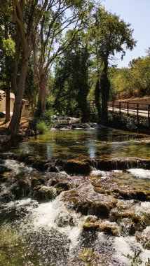 Güneşli bir yaz gününde, yemyeşil ağaçlarla çevrili Krka Ulusal Parkı 'ndaki kayaların üzerinde çağlayan küçük bir şelalenin manzarası.