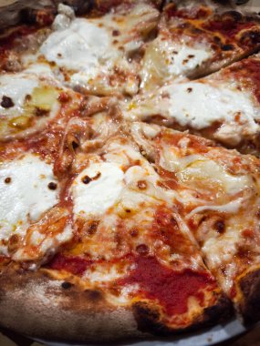 Yanan ahşap bir pizzanın yakınında köpüren peynirler ve mükemmel kavrulmuş bir kabuğun üzerinde zengin domates sosu İtalyan mutfağının özünü yakalıyor.