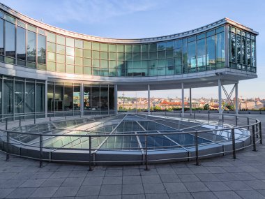 Prag, Çek Cumhuriyeti - 6 Mayıs 2025: Letna parkında cam kaplı bir binanın ön planda panoramik bir manzara sunan eğri camlı cephesi