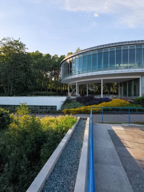 Prag, Çek Cumhuriyeti - 6 Mayıs 2025: Prag, Czechia 'da cam cepheli modern dairesel bina, yeşilliklerle çevrili, batan güneşin sıcacık ışığıyla aydınlanıyor