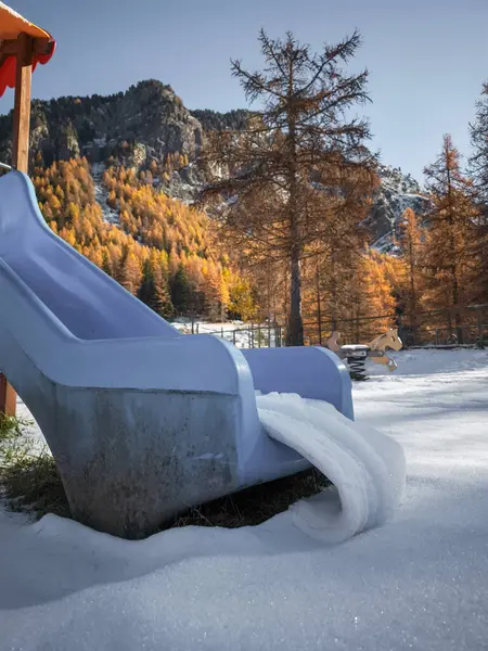 Mavi oyun alanı kısmen karla kaplı, Aosta, İtalya 'daki sonbahar ağaçları ve dağlara karşı Kasım ayında Frazionne Lillaz