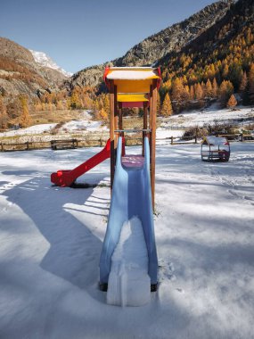 Aosta Vadisi 'nin sonbahar dağları ve ağaçları Frazionne Lillaz' ın manzaralı zeminine karla kaplanmış canlı oyun alanı kaydırağıyla kaplanmış.
