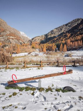 Kar, Aosta, İtalya 'da bir tahterevalliyi örtüyor. Etrafı sonbahar ağaçları ve görkemli dağlarla çevrili. Açık mavi bir gökyüzü altında Frazionne Lillaz.