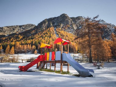 İtalya 'nın Aosta kentindeki kar tozlu dağların ve sonbahar yapraklarının arkaplanına kurulmuş renkli oyun alanı, sakin Kasım ayı manzarası Frazionne Lillaz' ı yakalıyor.