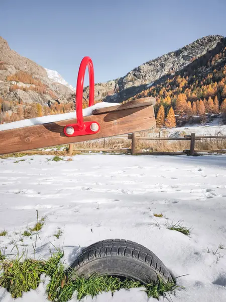Karla kaplı çocuk parkı tahterevalli dağ manzarasından önce dinleniyor, aosta vadisi kışın sakin gelişini yakalıyor canlı mavi gökyüzüne karşı Frazionne Lillaz