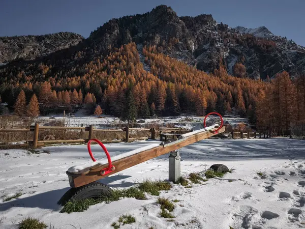 Tahta tahterevalli, Kasım Frazionne Lillaz döneminde İtalya 'nın Aosta kentindeki sonbahar ağaçları ve görkemli dağlarla çevrili karla kaplı yerde dinlenir.