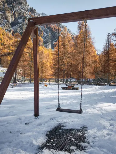 Salıncak seti, İtalya, Aosta 'da sonbahar ağaçlarıyla çevrili karlı bir oyun alanında duruyor. Dağlık bir bölgedeki mevsimlerin zıtlığını gözler önüne seriyor.