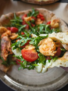 Taze karides, roka ve vişneli domatesle kaplanmış nefis bir pizzanın kapağı. Aosta, İtalya 'da canlı renkler ve dokular sergileniyor.