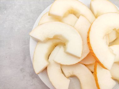 Olgun kanarya kavunu, canlı dilimler halinde güzel kesilmiş ve beyaz bir tabakta ustalıkla yerleştirilmiş, ferahlatıcı ve besleyici bir ikram sunuyor yaz atıştırmaları için mükemmel