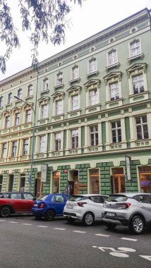 Prag, Czech Cumhuriyeti - 16 Eylül 2024: dekoratif cepheli ve birden fazla pencereli yeşil tarihi bina. Sokakta park etmiş arabalar.