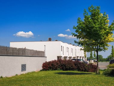 Prag, Çek Cumhuriyeti - 1 Mayıs 2025: Beyaz konut evleri, sazlık çitler, yapraklı bir ağaç ve açık mavi gökyüzü boşluğunun yer aldığı çağdaş konut mimarisi