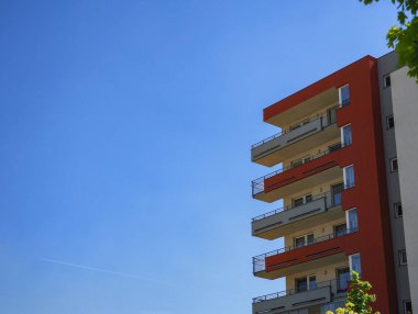 Canlı mavi gökyüzüne karşı balkonları olan modern apartman binası, çağdaş kentsel yaşam ve mimari tasarım kopyalama alanını temsil ediyor.