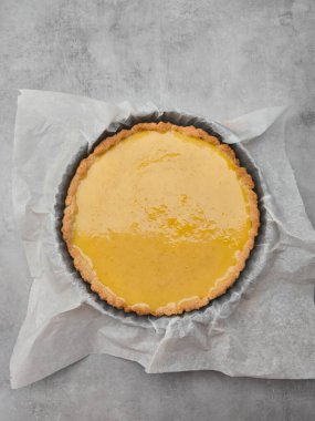 Taze pişmiş limonlu tart kek tepsisindeki kağıt üzerinde dinleniyor, canlı sarı bir renk sergiliyor ve tatlılığı davet ediyor, servis için hazır.