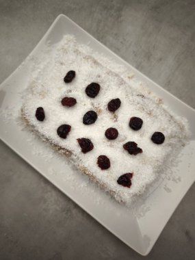 Hindistan cevizi gevreğiyle kaplı dikdörtgen noel pudingi ve kurutulmuş kızılcıklarla süslenmiş, aperatif olarak beyaz dikdörtgen bir tabak parti yemeği, Yeni Yıl arifesi yemeği, Noel ya da doğum günü yemeği