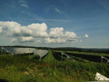 Cesky Krumlov, Çek Cumhuriyeti - 6 Temmuz 2024: Güneş panelleri dolni dvoriste 'de kabarık bulutlu, canlı mavi bir gökyüzü altında yemyeşil bir alan boyunca uzanıyor, yenilenebilir enerji sergiliyor.