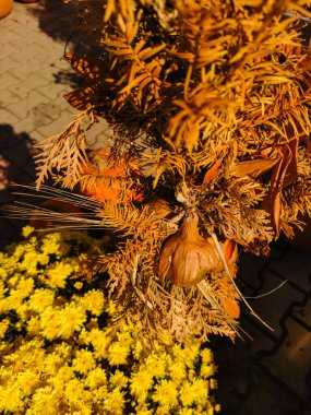 Sıcak ve kırsal bir atmosfer oluşturan kurumuş bitkiler ve çiçeklerden oluşan bir bileşim, canlı sarı kasımpatıların yanında balkabaklarını da barındırarak, sonbaharın samimi cazibesinin özünü yakalıyor.