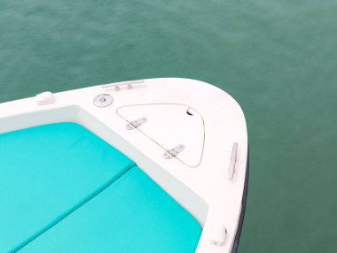 Turkuaz minderlerin, metal tesisatların ve sakin yeşil sularda yüzen küçük bir kapağın bulunduğu beyaz bir motorlu teknenin pruvasını kapatın.