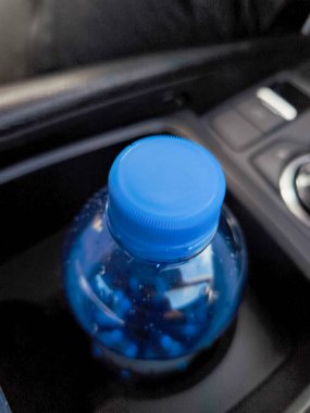 Mavi haplar mavi kapaklı plastik bir şişenin içinde saklanır. Arabanın bardak tutacağına yerleştirilir. Bu da potansiyel bir sağlık veya seyahatle ilgili bir konsept olduğunu gösterir.