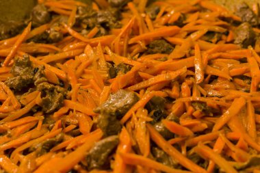 Geleneksel Özbek yemek pilavının, taze et ve turuncu havuçlarla yakın plan görüntüsü, bu lezzetli mutfağın canlı renklerini ve dokularını vurguluyor, kültürel zenginliği çağrıştırıyor.