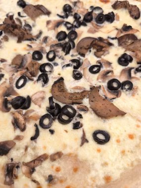 Close up of a freshly baked pizza featuring a generous topping of mushrooms and black olives on a creamy white sauce