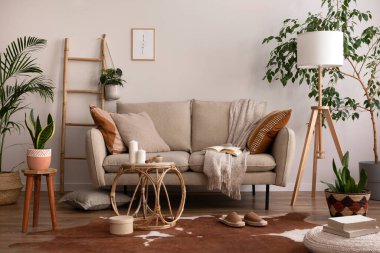 Kahverengi halı, yastık, ekose, kahve masası ve kişisel aksesuarlarla bej koltuklu oturma odasının şık kompozisyonu. Poster çerçeveli bej bir duvar. Ev dekoru. Şablon. 