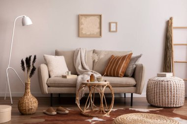 Kahverengi halı, yastık, ekose, kahve masası ve kişisel aksesuarlarla bej koltuklu oturma odasının şık kompozisyonu. Bej renkli duvar ve sahte poster. Ev dekoru. Şablon.