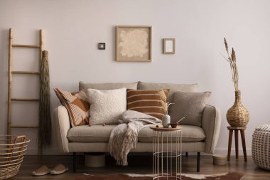 Kahverengi halı, yastık, ekose, kahve masası ve kişisel aksesuarlarla bej koltuklu oturma odasının şık kompozisyonu. Bej renkli duvar ve sahte poster. Ev dekoru. Şablon.