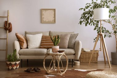 Kahverengi halı, yastık, ekose, kahve masası ve kişisel aksesuarlarla bej koltuklu oturma odasının şık kompozisyonu. Bej renkli duvar ve sahte poster. Ev dekoru. Şablon.