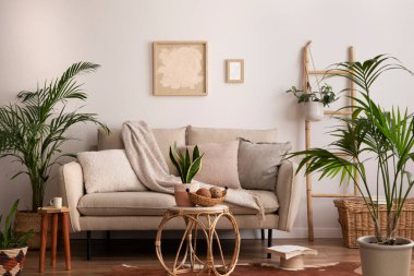 Oturma odasının içi bej kanepe, yastıklar, poster çerçeveleri, rattan kahve masaları, bitkiler, bambu merdiveni, dekorasyon ve kişisel aksesuarlarla dolu. Ev dekoru. Şablon.