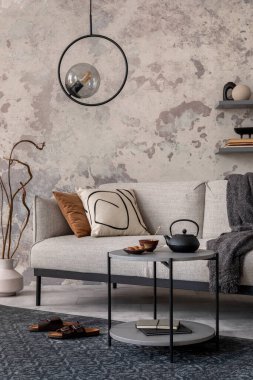 Tasarım gri kanepe, halı, yuvarlak lamba, siyah sehpa, dekorasyon, yastık ve zarif aksesuarlarla oturma odasının zarif ve modern kompozisyonu. Beton grunge duvar.
