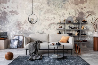 Gri dizayn kanepesi, sehpası, kitaplığı, gösterişli lambası, halısı, dekorasyonu ve zarif aksesuarları olan modern dairenin çatı katı tarzı. Beton grunge duvar. Şablon.