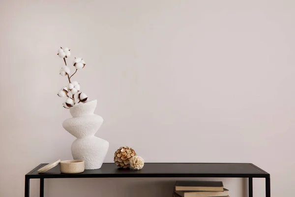 Minimalist composition of minimalistic interior with copy space. White vase with dried flowers and stylish accessories. Beige wall. Home decor. Template.