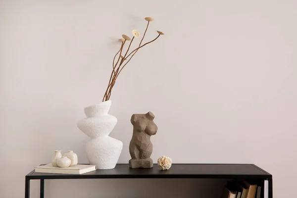 Minimalist composition of minimalistic interior with copy space, beige wall, white vase with dried flowers, sculpture and stylish accessories. Home decor. Template.