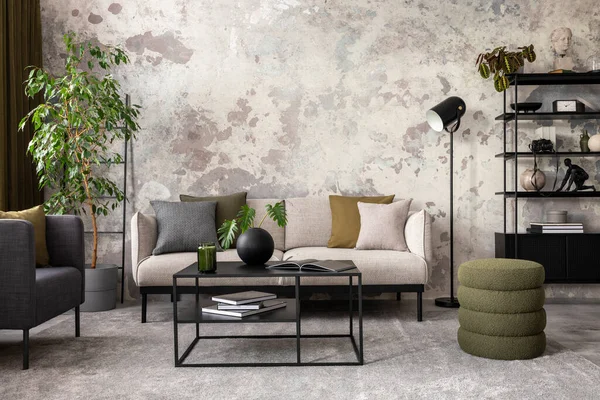 Creative composition of living room interior with gray sofa, stylish green pouf, black coffee table, rack, armchair, pillows, vase with dried flowers and personal accessories. Home decor. Template.