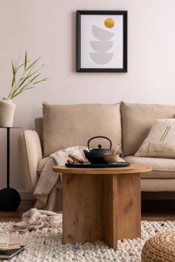 Bej kanepe, yastık, ahşap sehpa, poster çerçevesi, siyah çay tenceresi, sehpa ve zarif dekorasyonlu şık oturma odasının yaratıcı kompozisyonu. Sıcak ev dekorasyonu. Şablon.