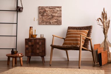 Oturma odasının içi sıcak ve rahat. Poster çerçevesi, ahşap büfe, kurumuş çiçekli cam vazo, bej halı, kahverengi koltuk ve kişisel aksesuarlar. Ev dekoru. Şablon. 