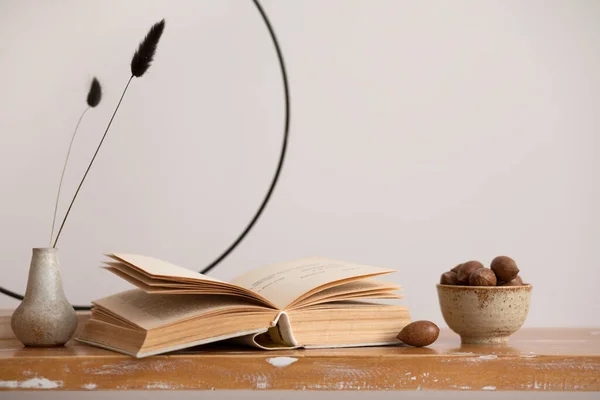 The minimalistic composition of interior with book, vase with dried flowers and almonds. Home decor. Template.