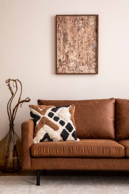 Poster çerçevesi, kahverengi kanepe, bej halı, desenli yastık, kurumuş çiçekli cam vazo, dekorasyon ve şık kişisel aksesuarlarla modern oturma odası kompozisyonu. Ev dekoru. Şablon.