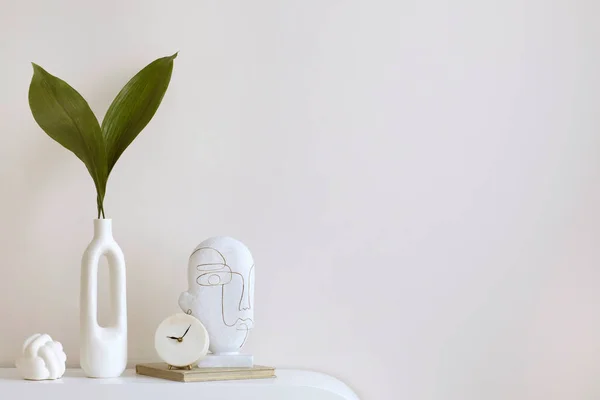 Minimalist composition of elegant and outstanding space with copy space, white vase with leaves, clock, book, sculpture and personal accessories. Home decor. Template.
