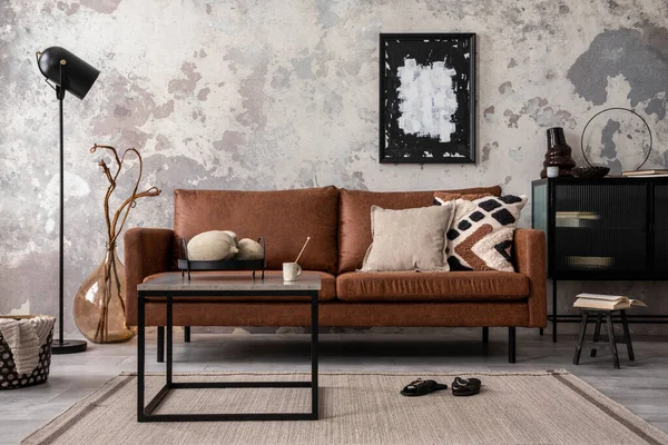 Interior design of loft industrial apartment with mock up poster frame, modern brown sofa, square coffee table, black commode and stylish personal accessories. Concrete gray wall. Home decor. Template.