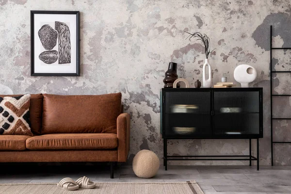 Interior design of loft industrial apartment with mock up poster frame, brown sofa, carpet, black commode patterned pillow and personal accessories. Gray concrete wall. Home decor.