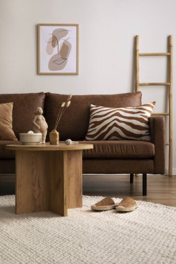 Warm and cozy interior of living room space with brown sofa, round beige carpet, wooden coffee table, mock up poster frames, decoration and elegant personal accessories. Cozy home decor. Template.