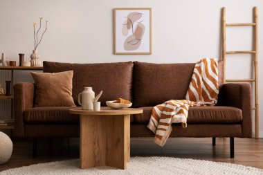 Warm and cozy interior of living room space with brown sofa, round beige carpet, wooden coffee table, mock up poster frames, decoration and elegant personal accessories. Cozy home decor. Template.