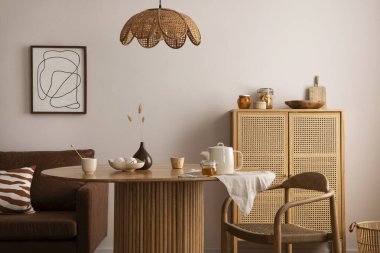 Boho and cozy interior of dining room with round wooden table, design chair, brown sofa, shelf, mock up poster frame, pendant lamp, tea pot, decoration and elegant accessories. Stylish home decor. 