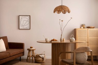 Boho and cozy interior of dining room with round wooden table, design chair, brown sofa, shelf, mock up poster frame, pendant lamp, tea pot, decoration and elegant accessories. Stylish home decor. 